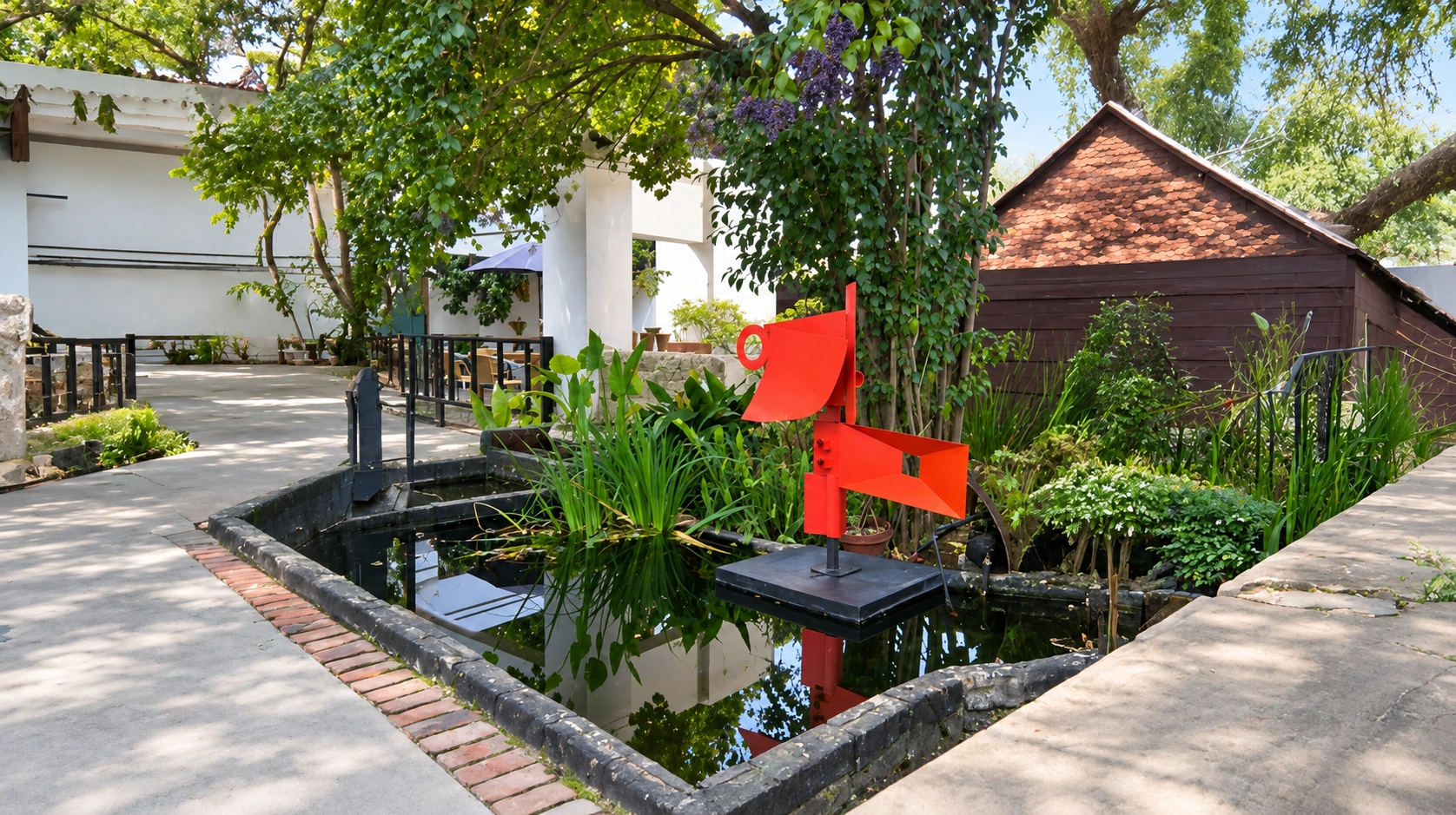 A red abstract metal sculpture standing above a garden pond